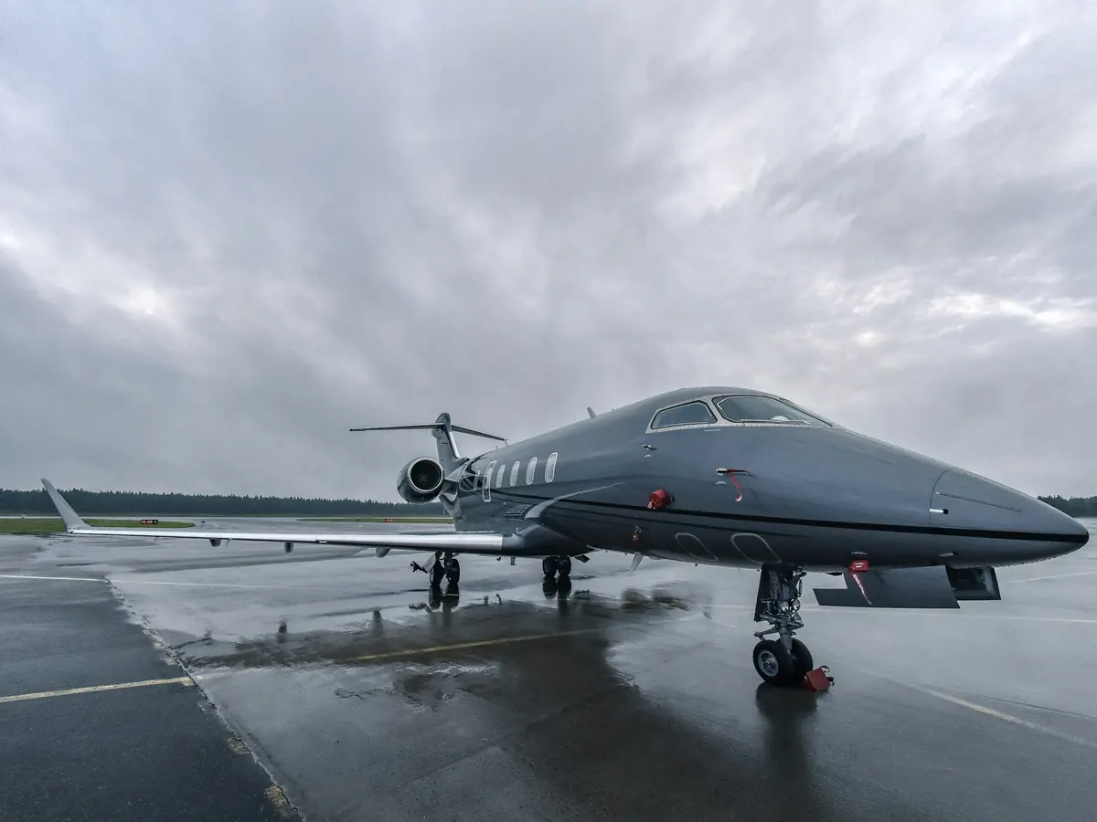 Dark grey super-midsize jet on a rain-washed ramp